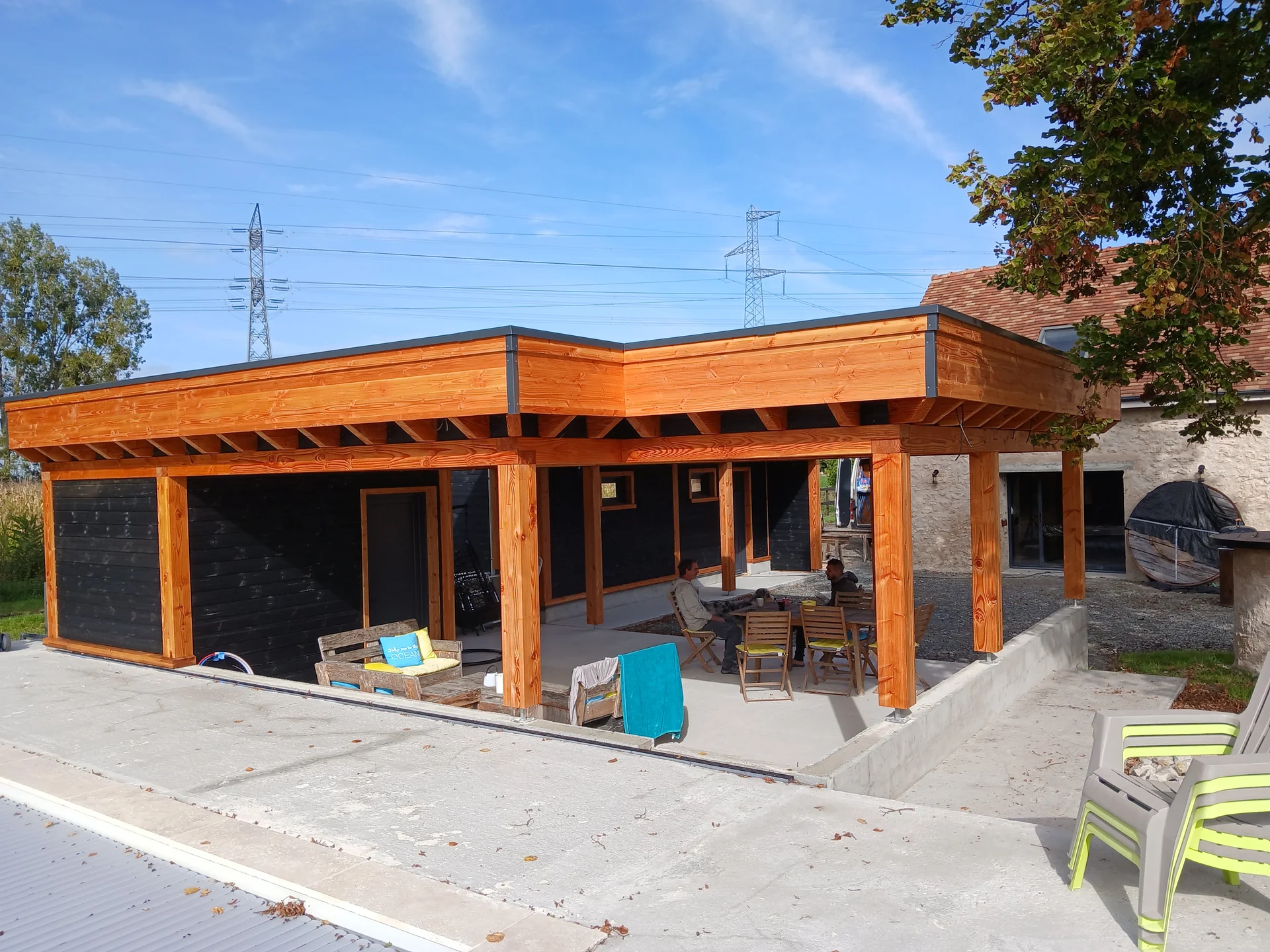 Terrasse couverte et poteaux en bois devant une construction à bardage foncé