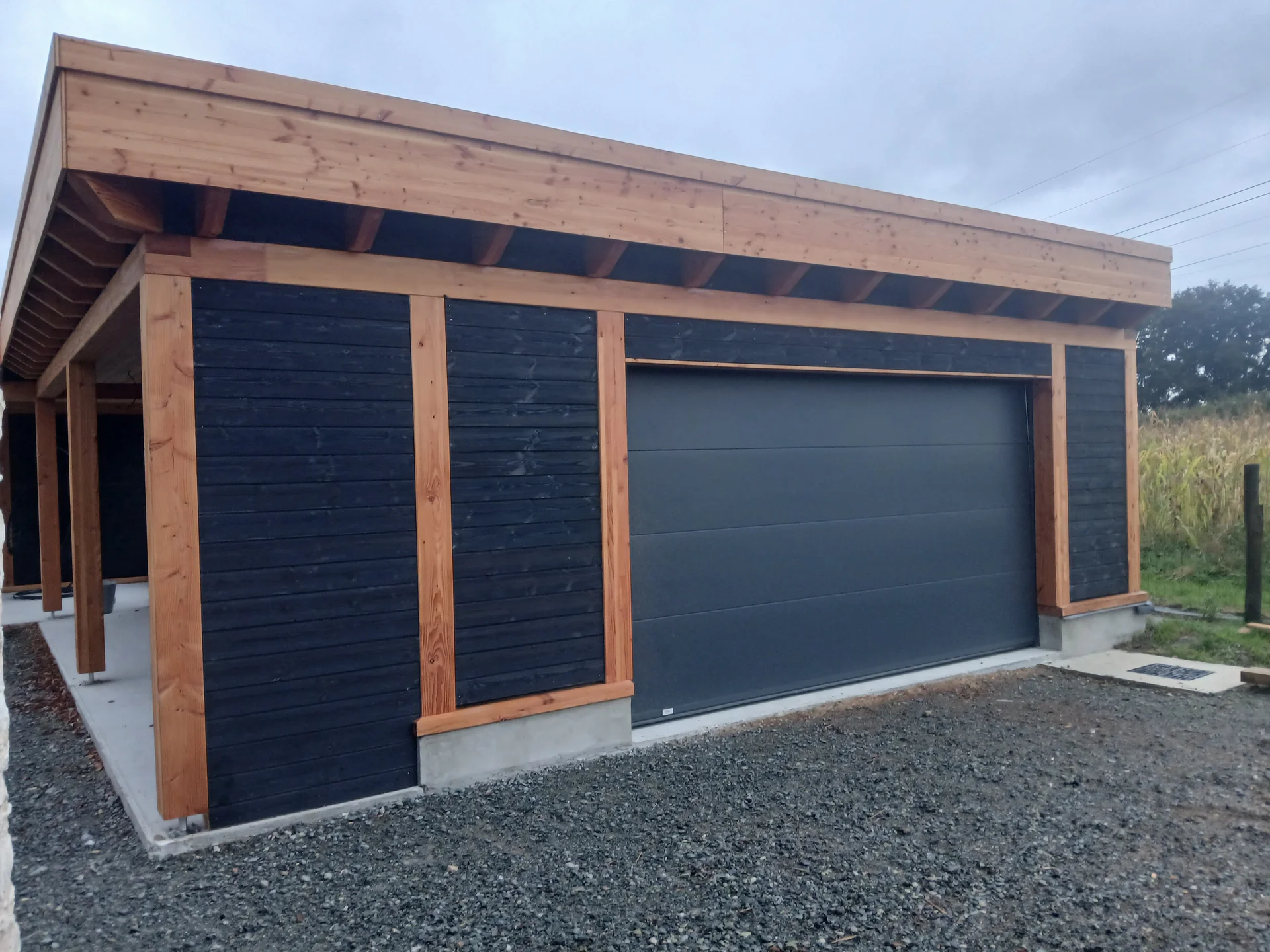Garage en bois avec bardage foncé et porte grise